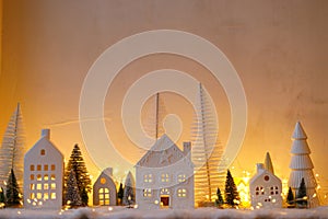 Atmospheric miniature christmas village. Stylish little white houses and trees on snow blanket with glowing lights in evening.