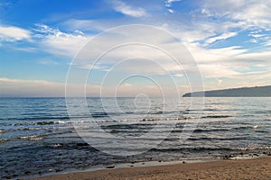 Atmospheric seascape. Blue sky with white clouds over the calm winter sea in a light evening haze, soft focus