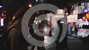 Atmospheric shot of happy Caucasian young local woman using smartphone app in dark busy New York night street crossing.