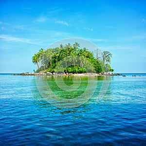 An atoll in the sea surrounded by blue sky and water with refle