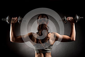 Atractive fit woman works out with dumbbells as a fitness conceptual over dark background