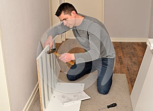 Atractive male assembling a cupboard usind hammer and screwdriver