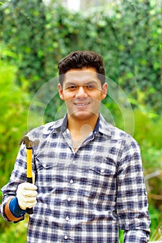 Atractive man wearing casual clothes holding a hammer in a forest background