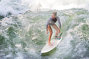 Atractive sporty girl surfing on famous artificial river wave in Englischer garten, Munich, Germany.