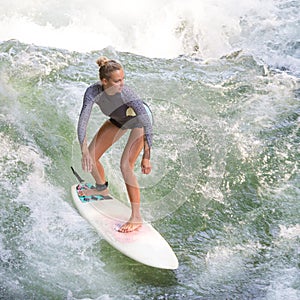 Atractive sporty girl surfing on famous artificial river wave in Englischer garten, Munich, Germany.