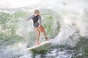 Atractive sporty girl surfing on famous artificial river wave in Englischer garten, Munich, Germany.