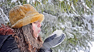 Atractive teen in hat blowing snowflakes