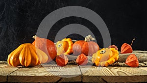 Atristic autumn rustic still life. pumpkins with squash and physalis on a rough burlap and boards against a dark concrete wall