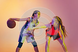 Attack and defense. Female basketball players, young girls, teen in action with basketball ball isolated on neoned