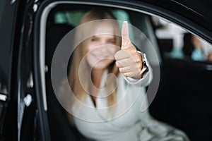 Attactive young bussines woman sitting in car in car showroom. Woman choosing new car. Beautiful blond hair female in