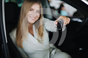 Attactive young bussines woman sitting in car in car showroom. Woman choosing new car. Beautiful blond hair female in