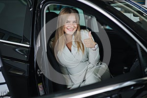 Attactive young bussines woman sitting in car in car showroom. Woman choosing new car. Beautiful blond hair female in