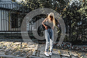 Attarctive calmy blonde girl in casual clothes stands near the green fence among the old city street