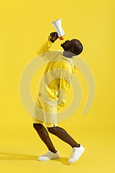 Attention! Black man shouting in megaphone on yellow background