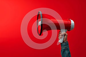 Attention grabbing image Hand holds megaphone against red background