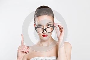 Attention listen to me. Close up portrait young woman wagging her finger holding glasses skeptically isolated white grey wall