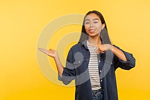 Attention, nice product advertise! Portrait of happy girl in denim shirt holding copy space with palm, pointing at empty place