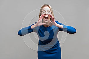 Attention! Portrait of aggressive woman holding her hands near wide open mouth.  on gray background