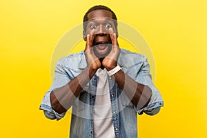 Attention! Portrait of scared man holding hands near wide open mouth and shouting. studio shot isolated on yellow background