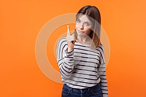 Attention! Portrait of worried young woman with brown hair in long sleeve striped shirt. indoor studio shot isolated on orange