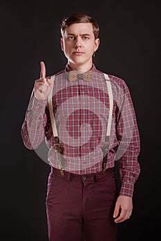 Attention! Strict Handsome young man in vintage shirt bow tie keeping finger raised and looking at camera while standing against