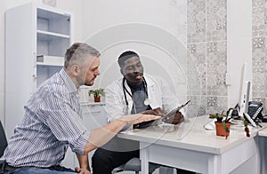 an attentive African-American doctor advises a patient during an appointment sitting at a table in a medical office.