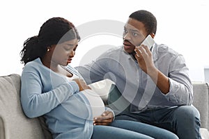 Attentive black husband calling doctor while wife having labor pains