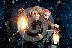 Attentive couple playing quest game while keeping hand lanterns against Christmas background. Couple outside with snow at night