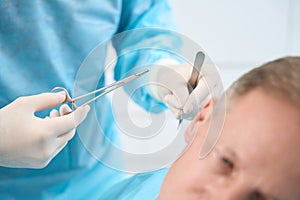 Attentive doctor in gloves preparing to put stitches on patient