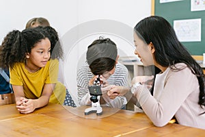 Attentive elementary schoolboy and Asian female teacher with microscopes in science classroom at school with friends. Education,