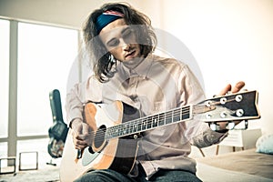 Attentive good-looking man with wavy hair tuning strings on acoustic guitar