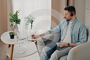 Attentive guy making notes in notebook during an online lesson at home