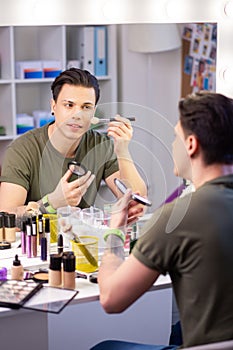 Attentive handsome man being busy with makeup products