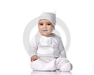 Attentive infant baby toddler in white jumpsuit overall and funny hat sits on the floor listens and tries to understand