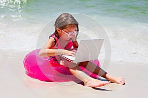 Attentive little girl sitting on beach with laptop