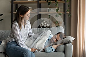 Attentive millennial wife carefully covering sleeping husband with warm blanket