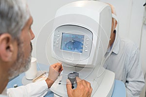 Attentive optometrist examining male patient on machine photo