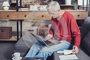 Attentive pensioner holding a laptop and paying for his bills online