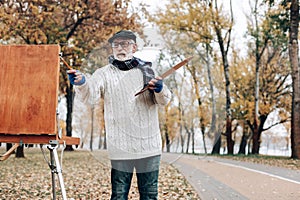 Attentive pensioner standing near his wooden easel