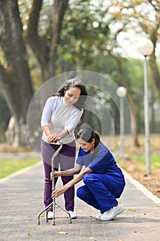 Attentive practitioner nurse assisting senior female walking with tripod cane. Assistance, rehabilitation and health
