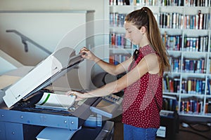 Attentive schoolgirl using Xerox photocopier in library photo