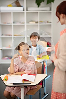 Attentive schoolgirl wearing pink dress listening to teacher