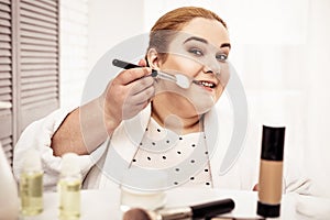 Attentive smiling plus-size woman using cosmetic brush