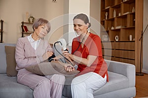 Attentive woman healthcare worker taking blood pressure of senior woman