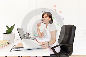 Attentive young caucasian female employee doing accounting paperwork in light modern office.
