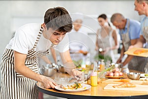 Attentive young man attendee of cooking course decorating meal made of salmon fish