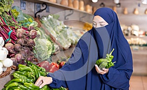 Attentive young Muslim woman purchaser choosing peppers in grocery store