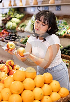 Attentive young woman purchaser choosing apples in grocery store
