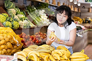 Attentive young woman purchaser choosing bananas in grocery store