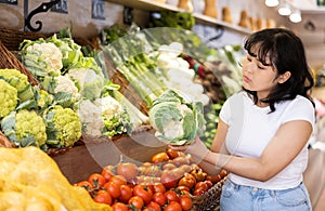 Attentive young woman purchaser choosing cabbage in grocery store